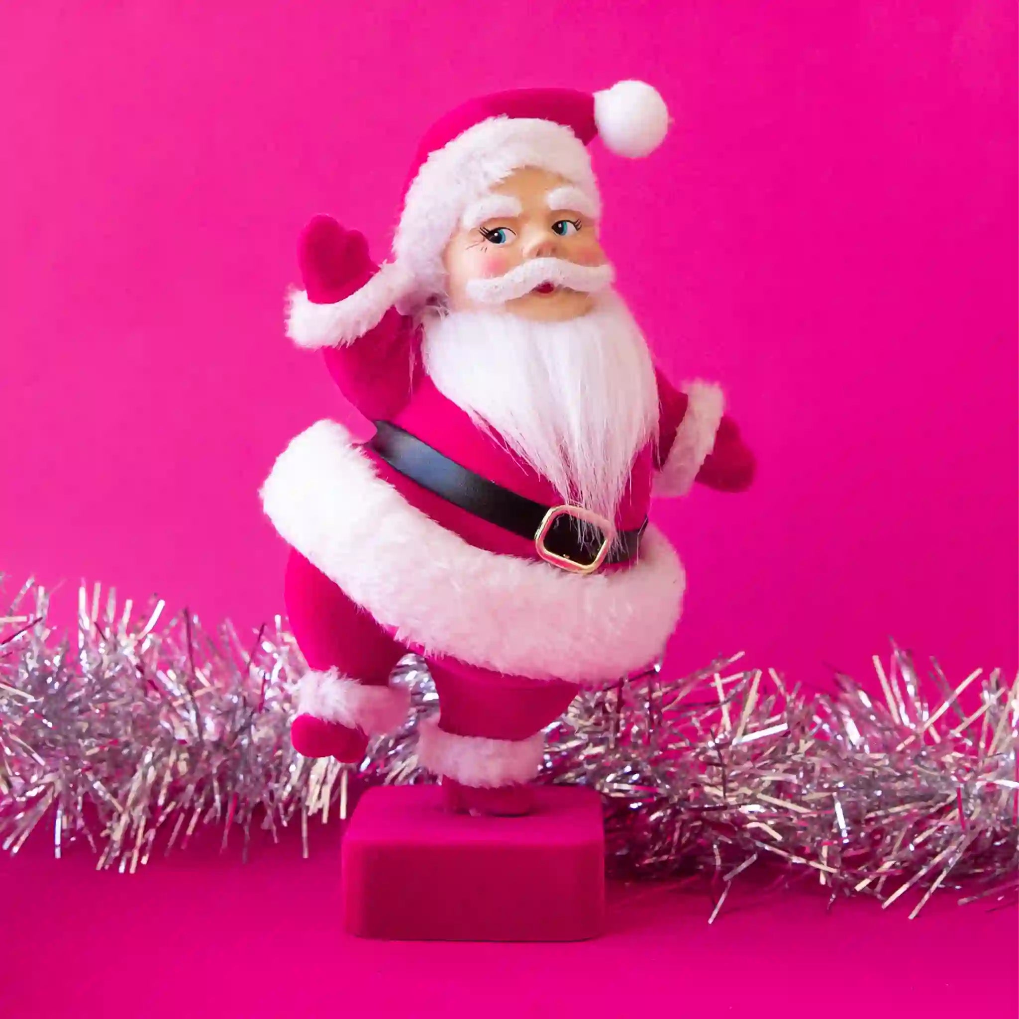 On a hot pink background is a hot pink flocked Santa shaped figurine holding a dancing pose.