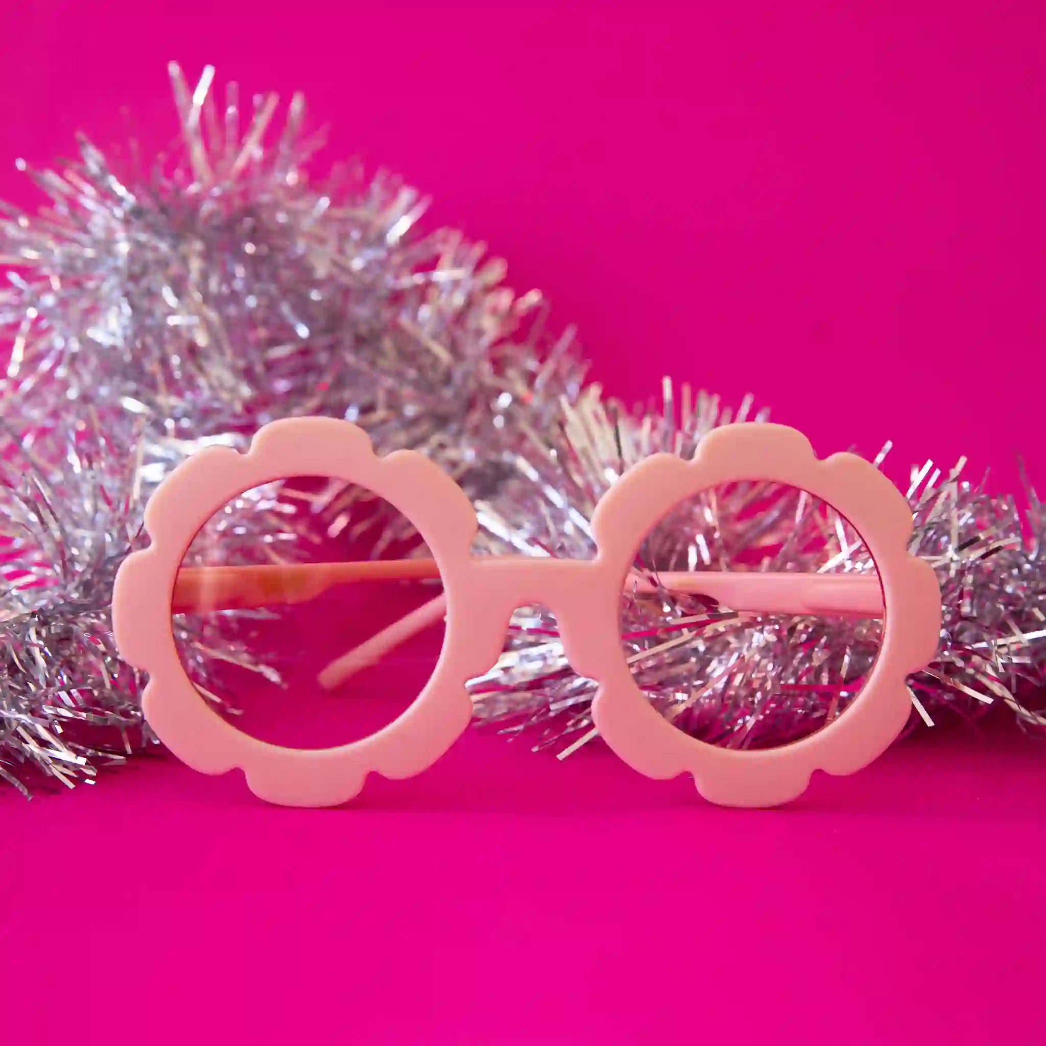 On a pink background is a light pink pair of flower shaped sunglasses with a light pink lens.