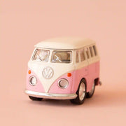 On a peachy background is a mini pink and white VW bus toy.