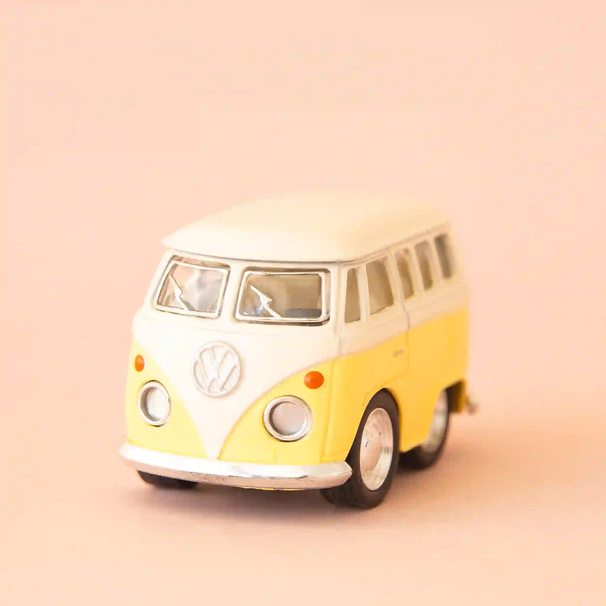 On a peach background is a yellow VW bus toy. 