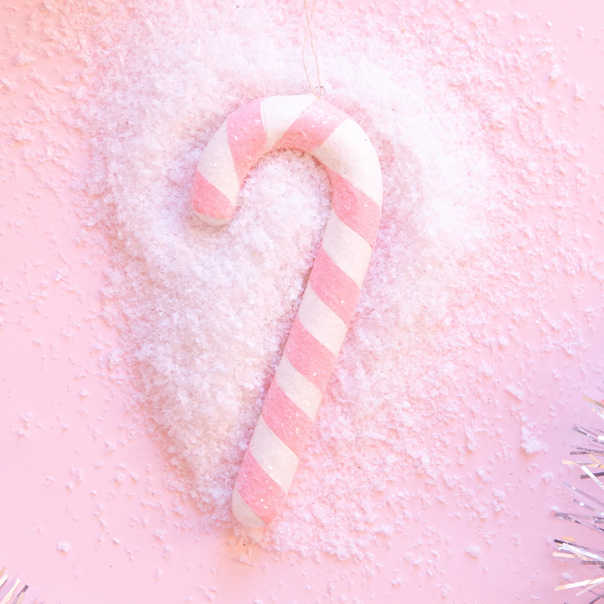 On a pink background is a light pink and white candy cane ornament.