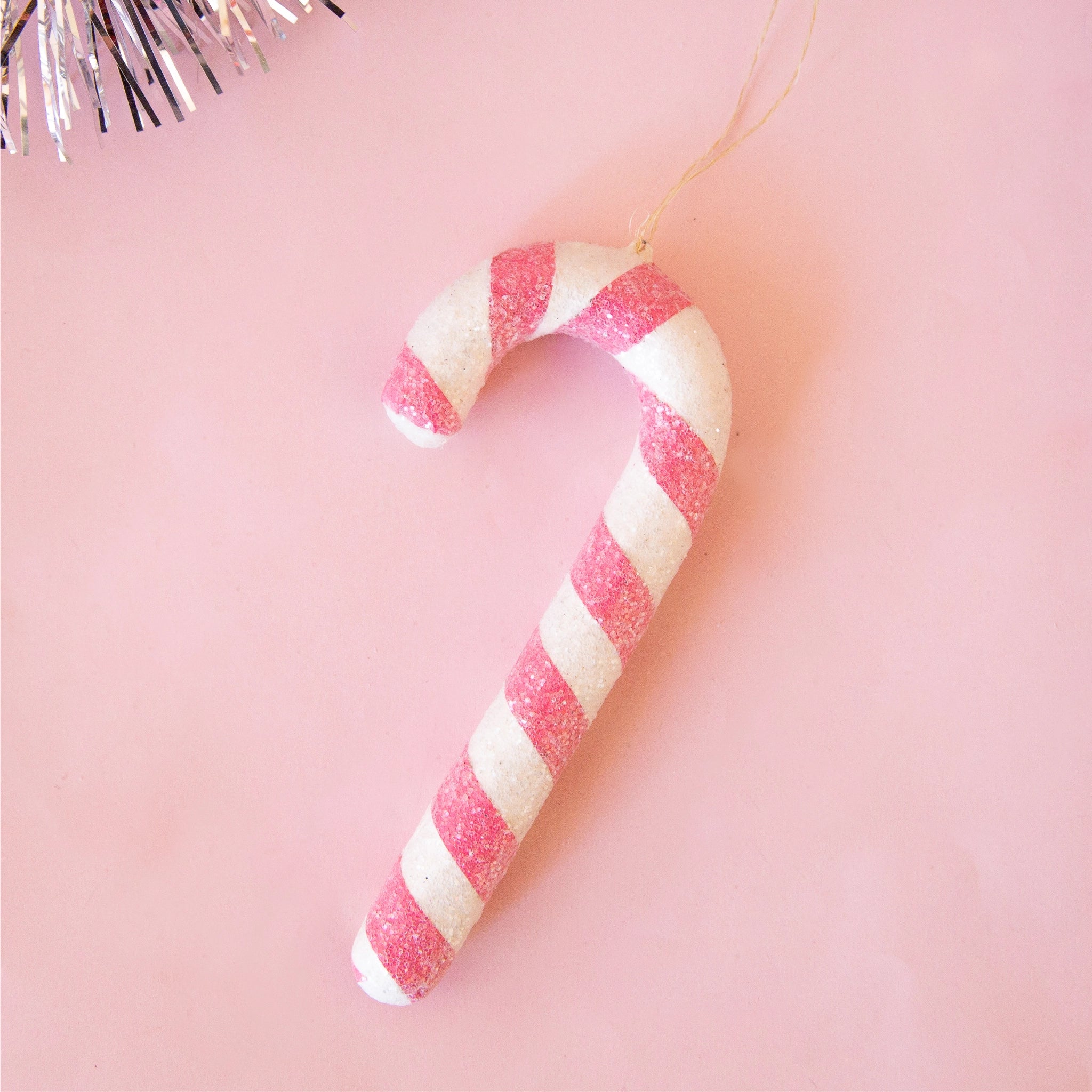 On a pink background is a white and pink candy cane shaped ornament. 