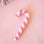 On a pink background is a white and pink candy cane shaped ornament. 
