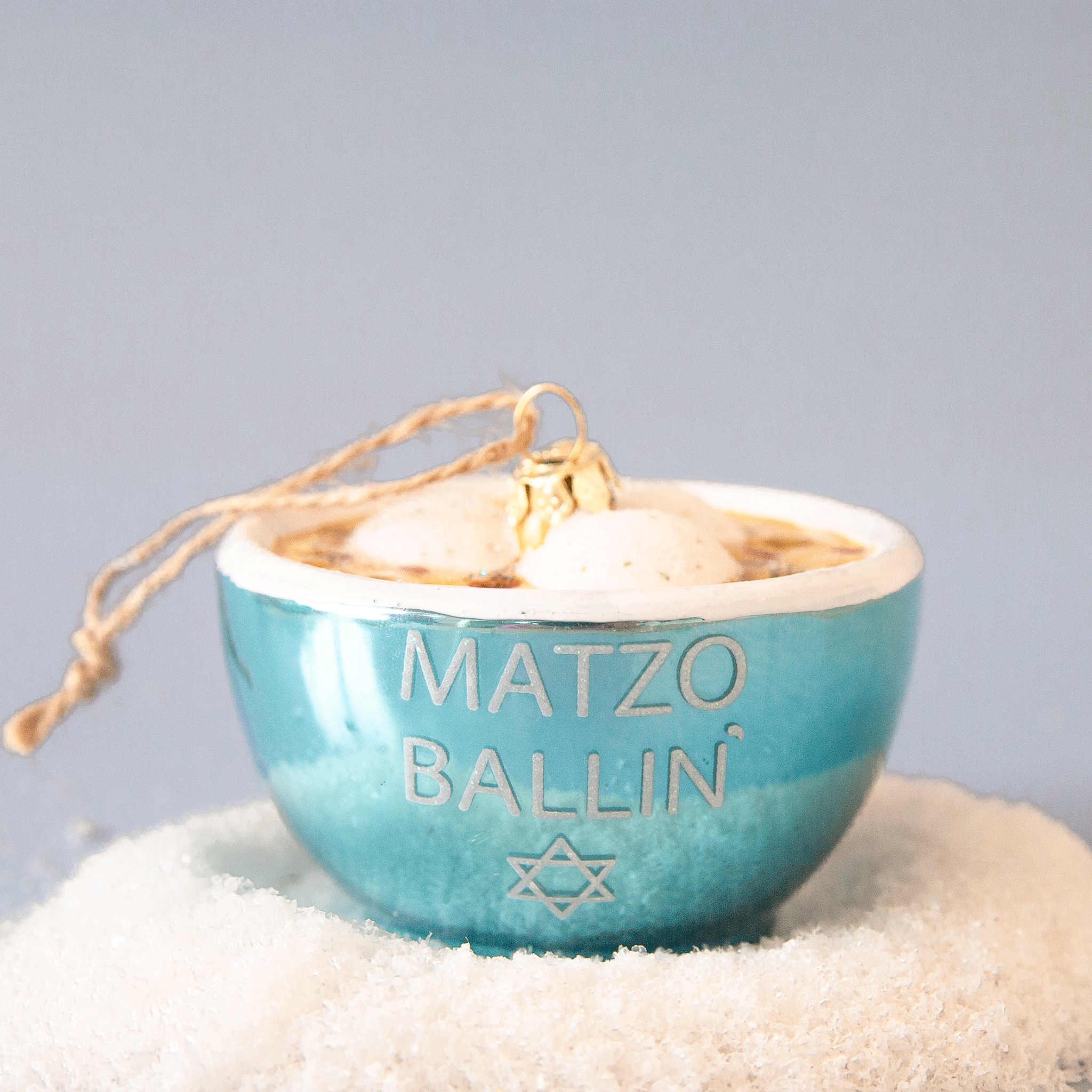 A glass matzo ball soup ornament with dumplings and a blue bowl that says "matzo ballin" in white text.