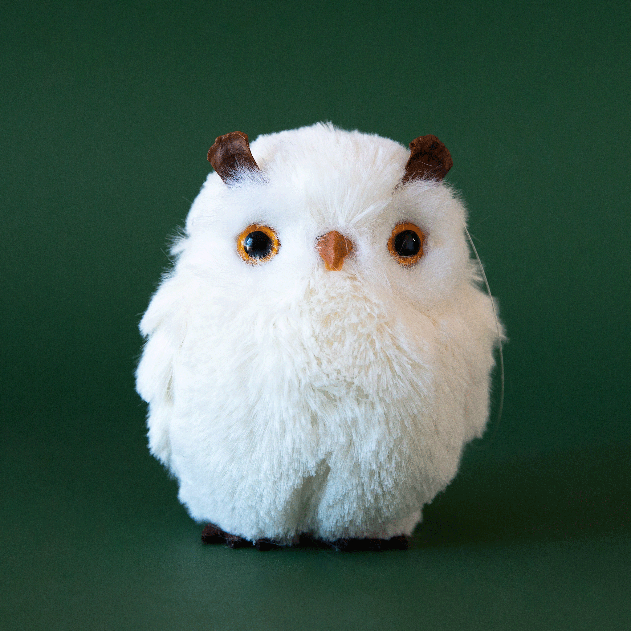 On a green background is a white fur owl ornament.