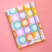  A spiral bound notebook with a multicolored checker design that has a white daisy in the center of each square. In the bottom right hand corner it says, "Creative Flow" in green text.