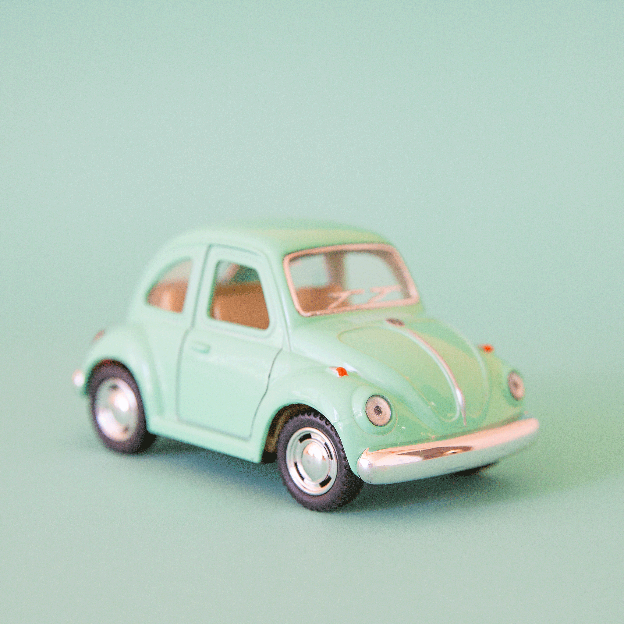 On a green background is a pastel green mini vw bug toy. 