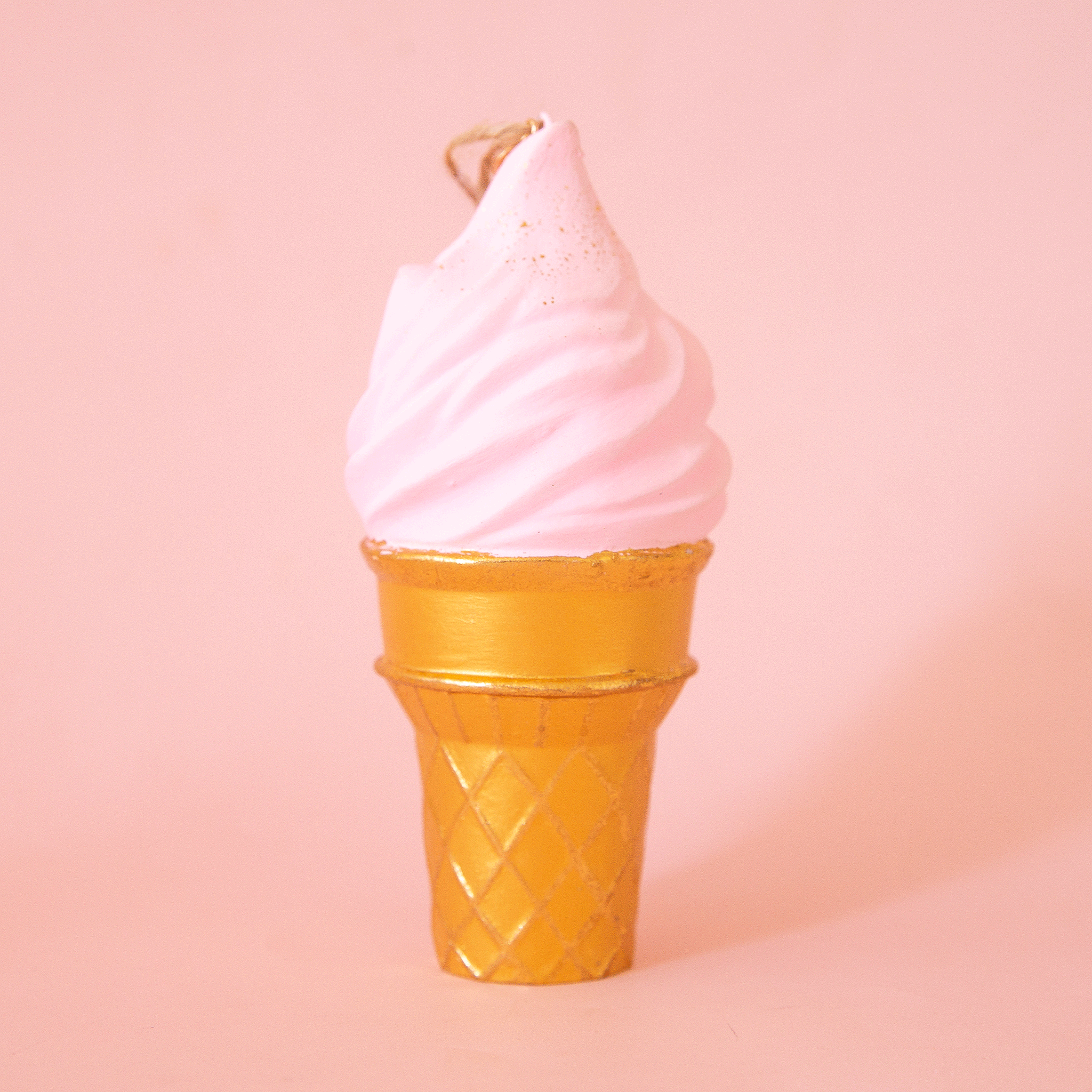On a pink background is a light pink ice cream cone shaped ornament. 