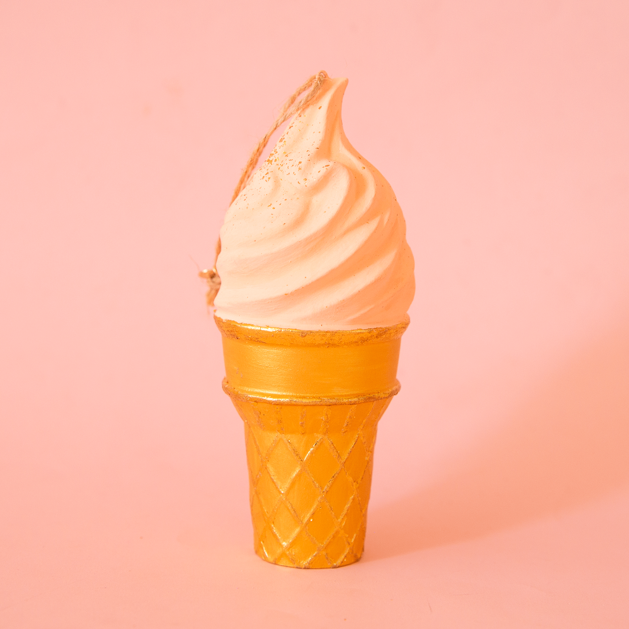 On a pink background is a light peach ice cream cone shaped ornament. 