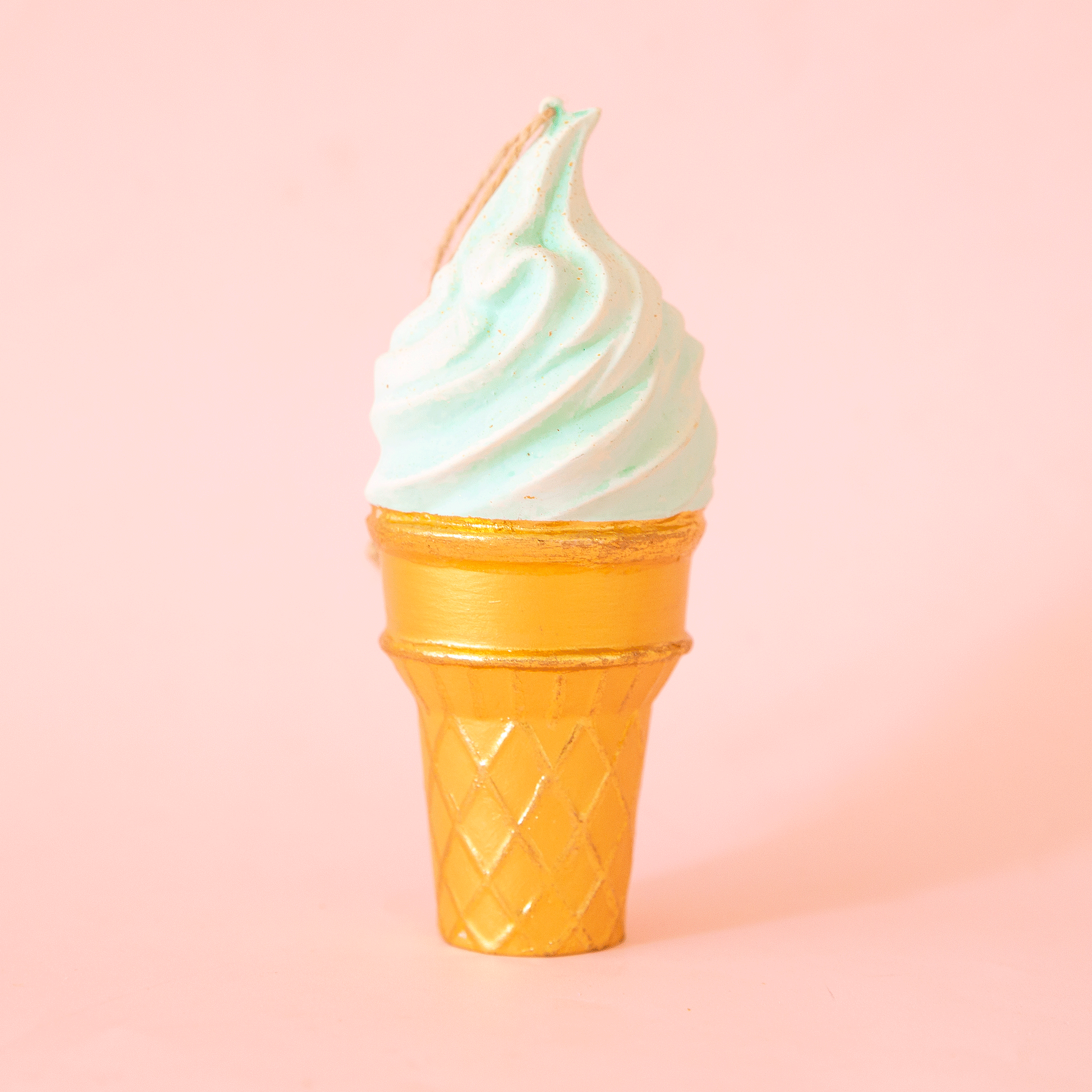 On a pink background is a mint green ice cream cone shaped ornament. 