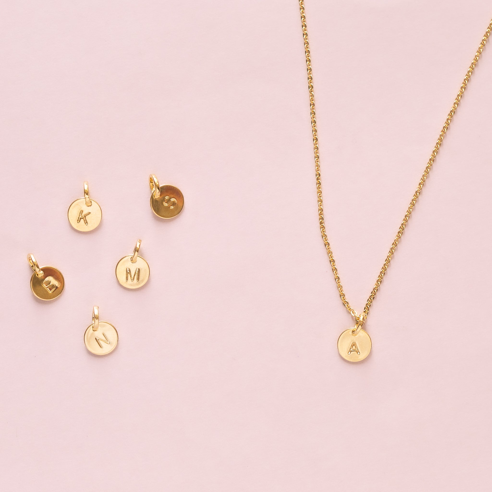 A dainty charm necklace with a circle charm that is engraved with an initial. 