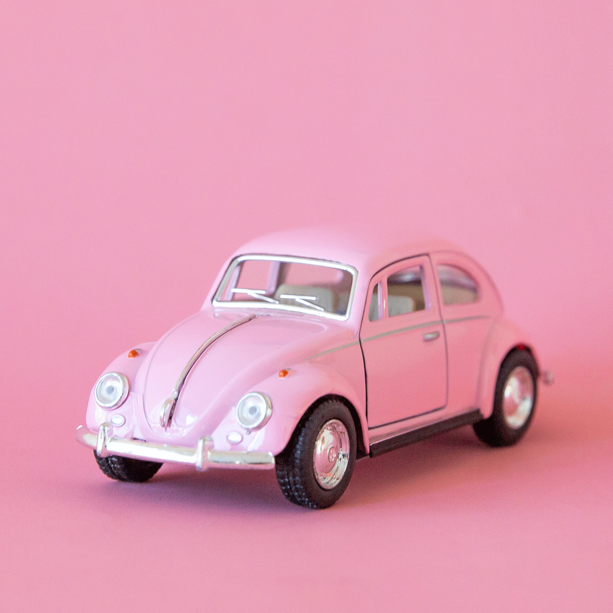 On a pink background is a pink VW bug toy. 
