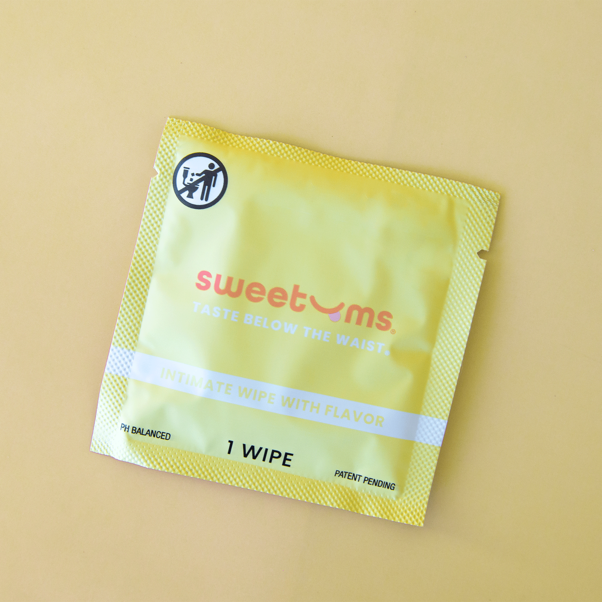 On a yellow background is a yellow packet of a single use feminine wipe with text on the front that reads, "sweetums taste below the waist".