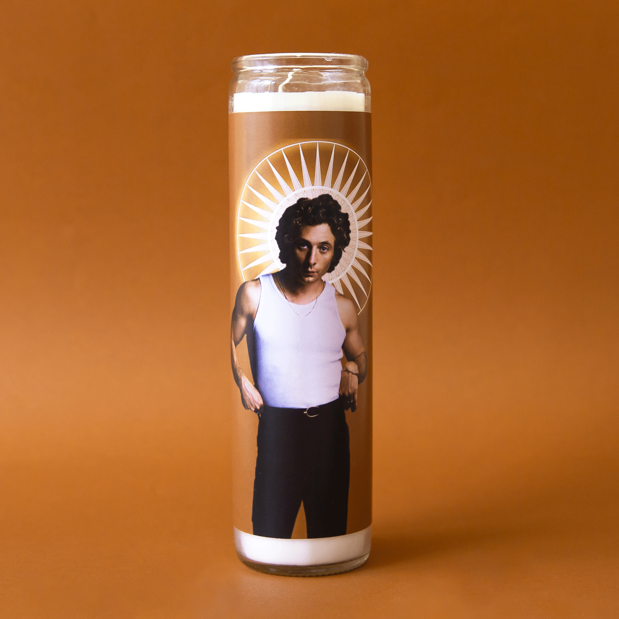 On an orange background is a thin, tall prayer candle with a photo of Jeremy Allen White on the front wearing a white tank top with black pants. 