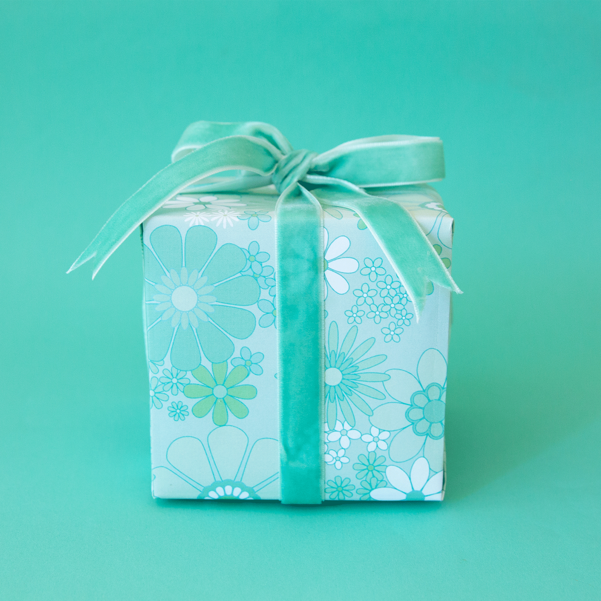 On a teal background is a gift box wrapped in a mint floral print wrapping paper with a velvet bow, not included with purchase. 