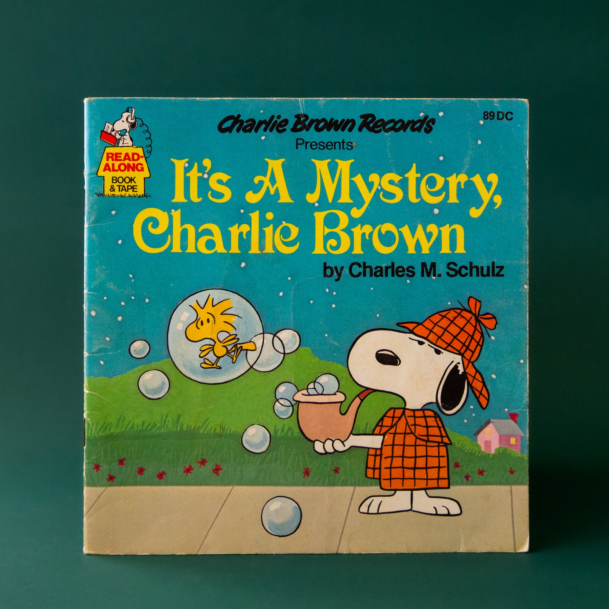 A book cover with Snoopy in a detective outfit and the title that reads, "Charlie Brown Records Presents It's A Mystery, Charlie Brown by Charles M. Schulz". 
