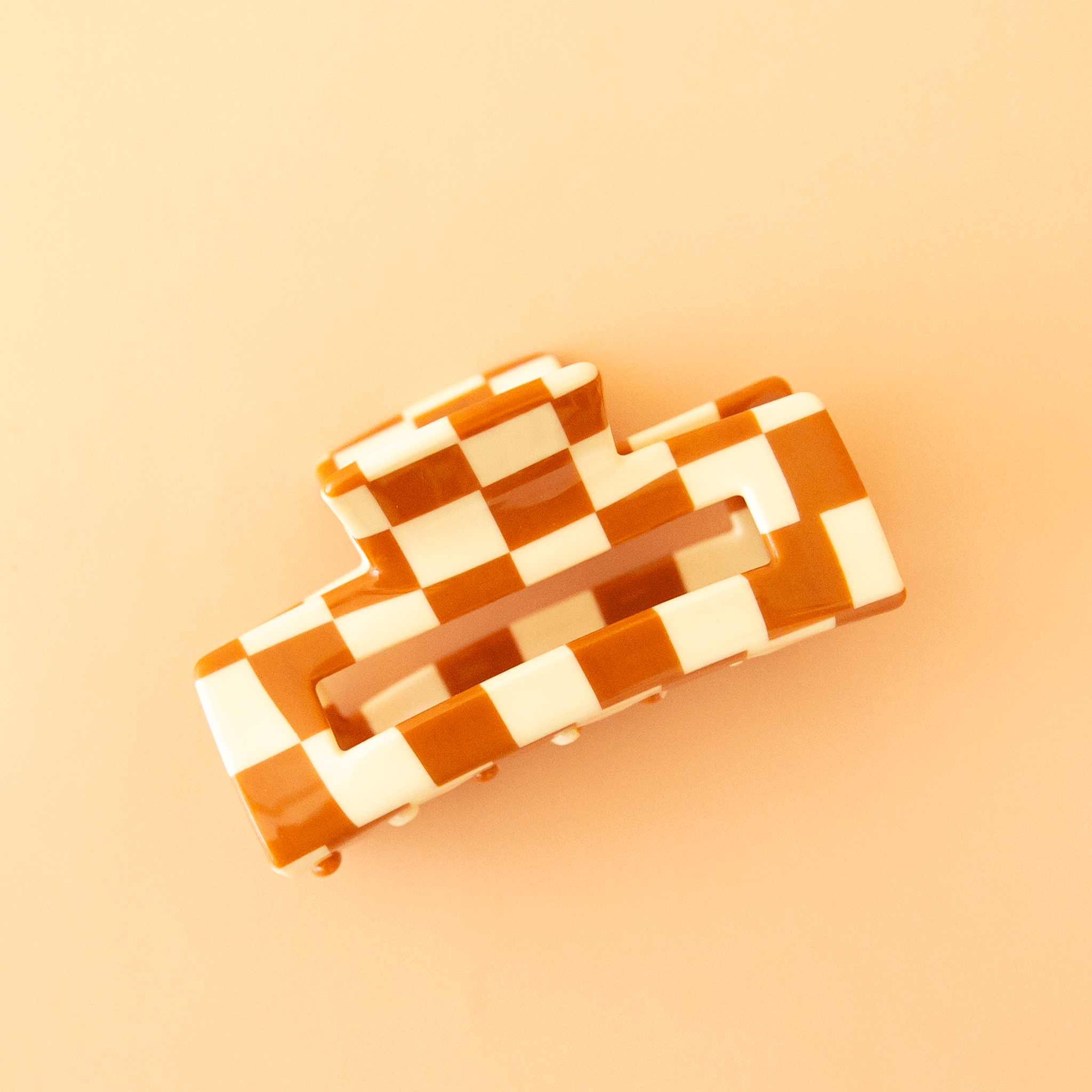On a tan background is an ivory and orange rectangle claw clip. 
