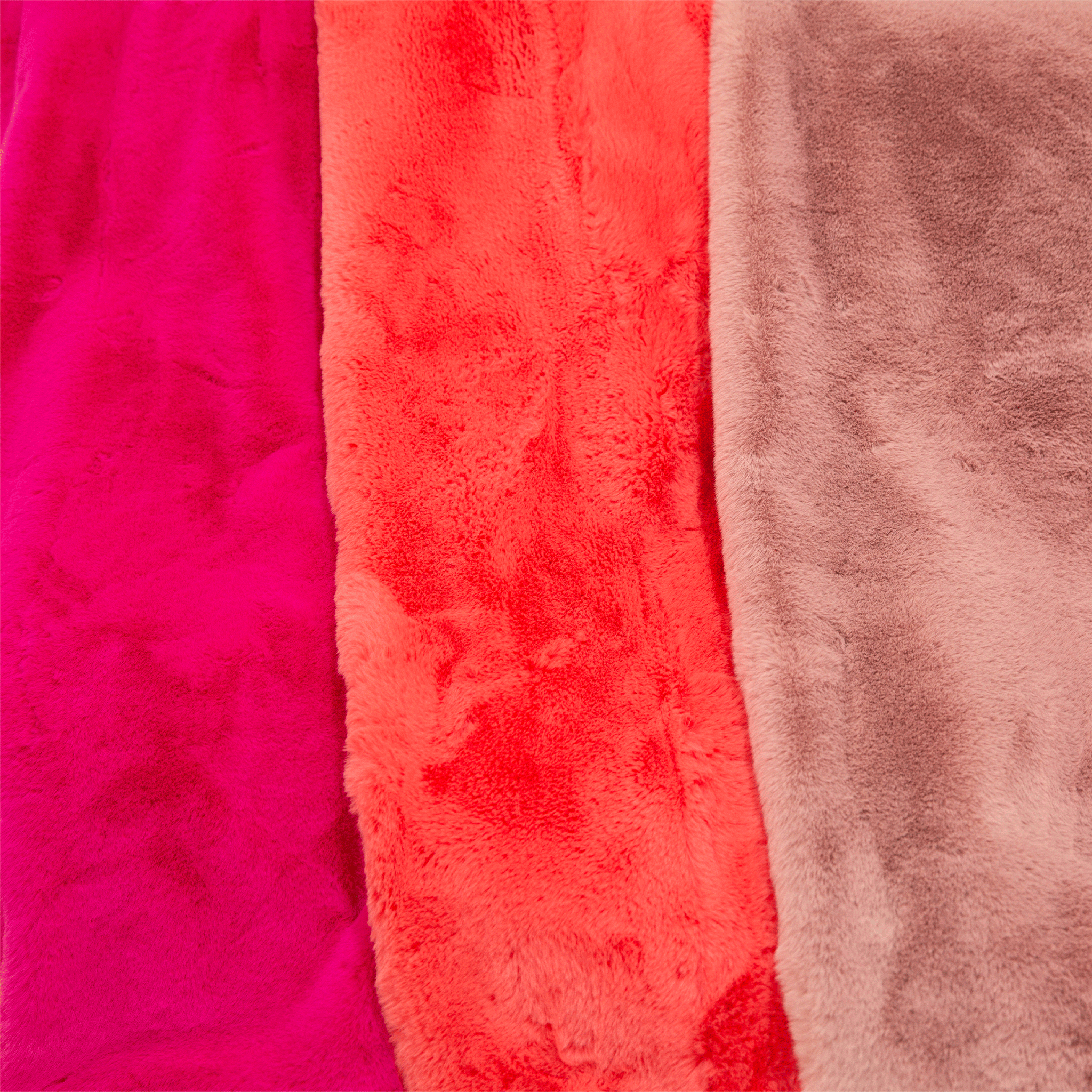 Three different shades of the luxe faux fur throw blankets next to one another. From left to right there is fuchsia, watermelon and dusty rose