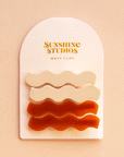 On a peach background is two pairs of wavy hair clips on a white arched cardboard backing with text at the top that reads, "Sunshine Studios Wavy Clips".