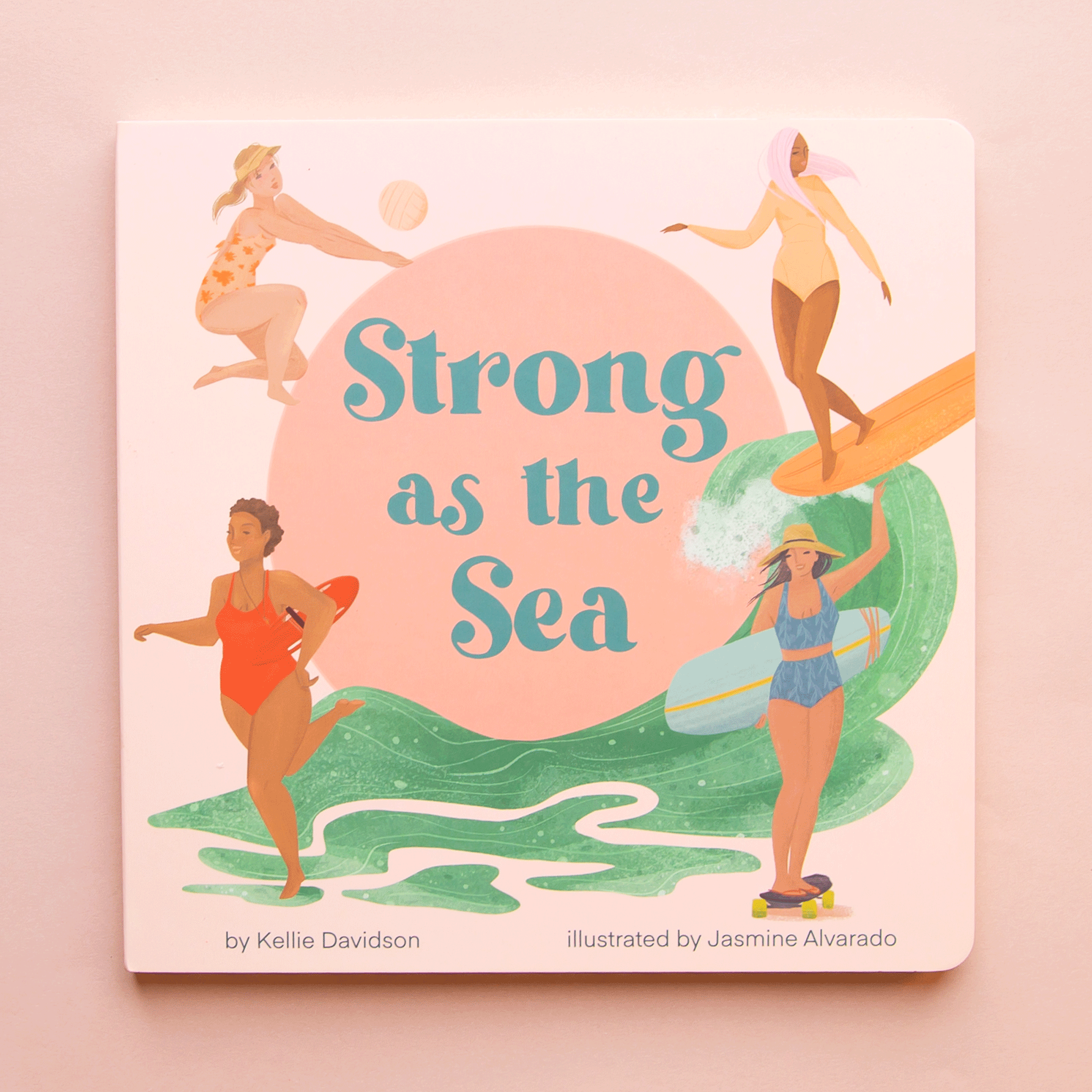 On a light pink background is a children&#39;s book with illustrations of four different women in each corner of beach themed book cover with blue text in the center that reads, &quot;Strong as the Sea&quot;.