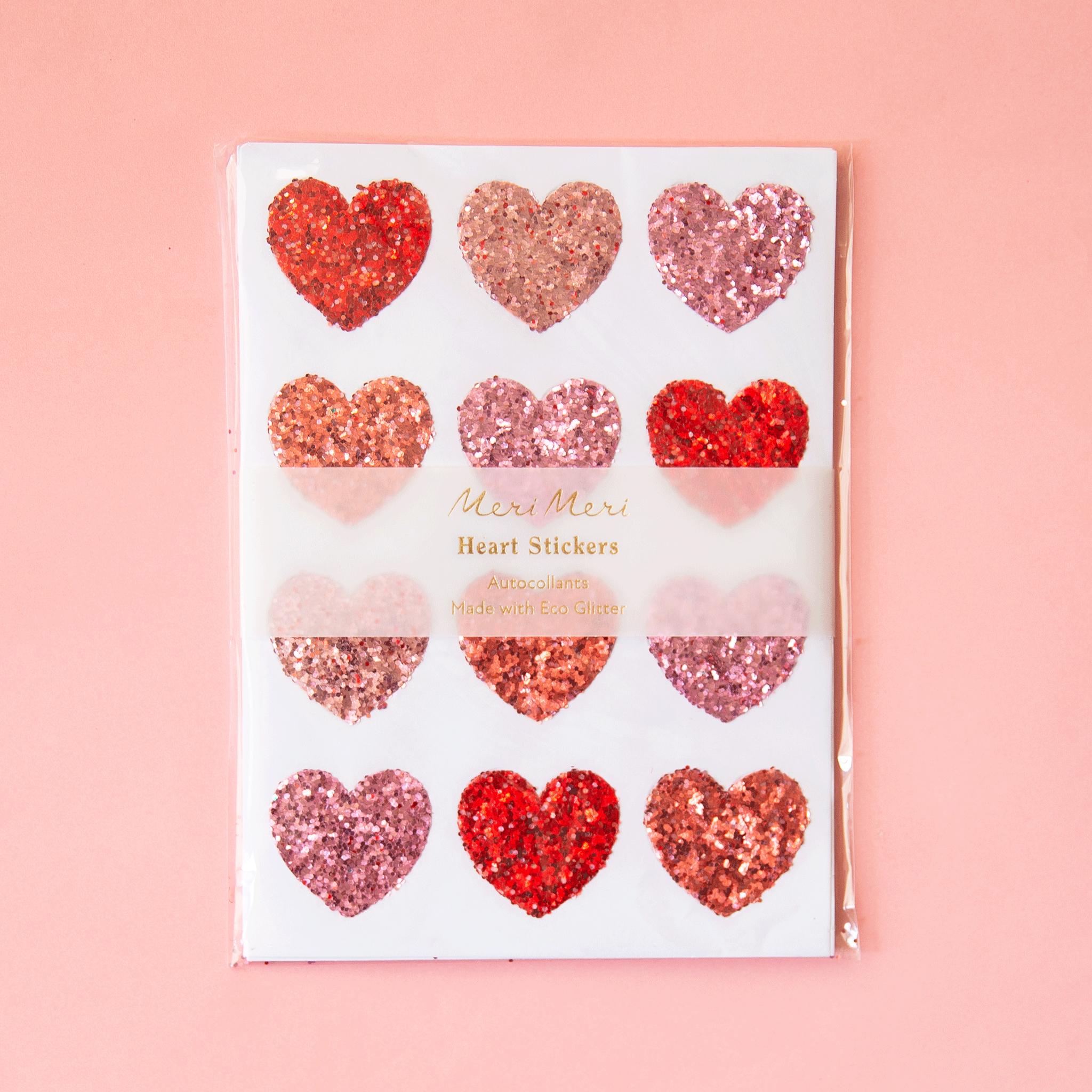 On a pink background is a sheet of heart shaped glitter stickers in shades of red and pink.