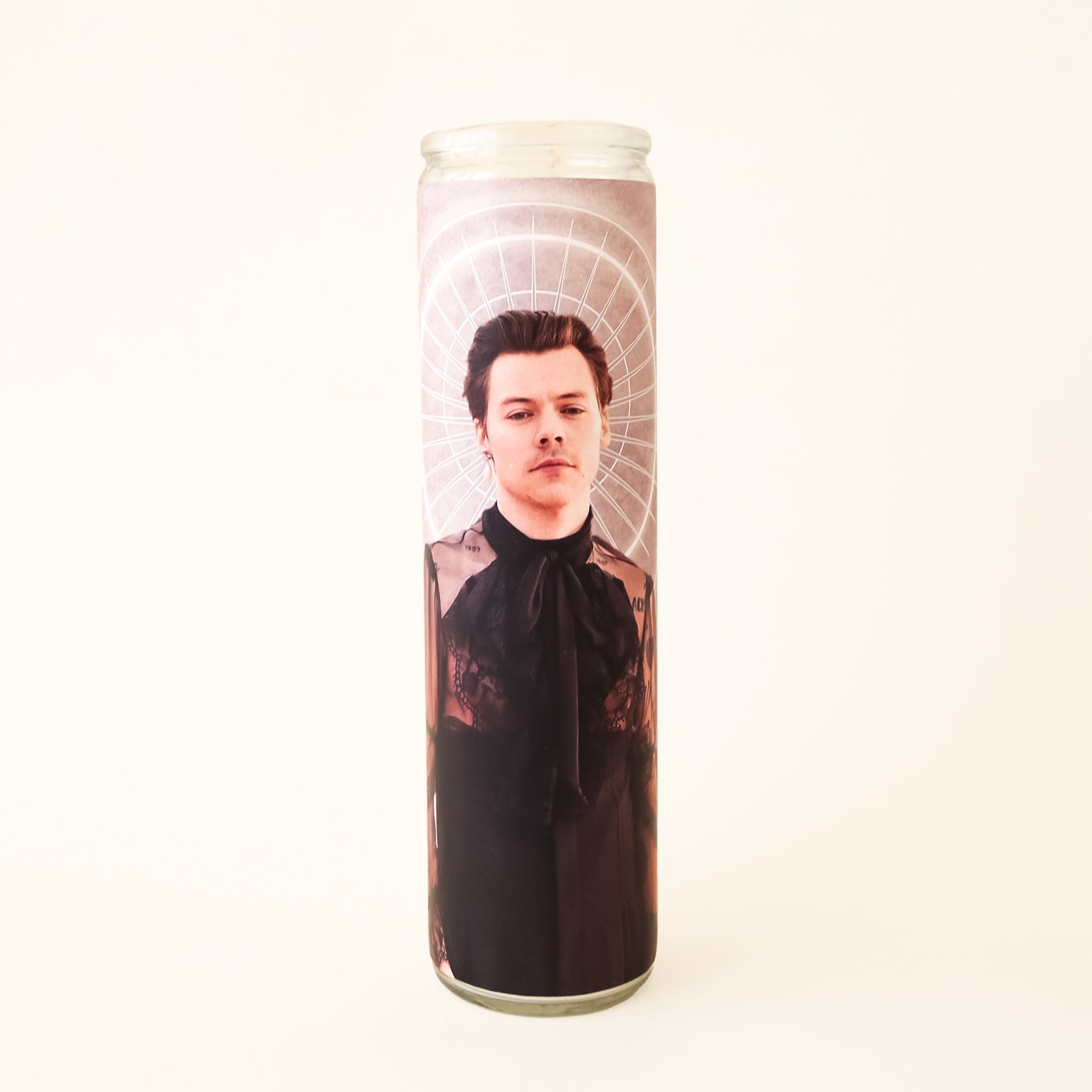 On a white background is a Harry Styles prayer candle and features a photo of him in his black lace ruffle top. 