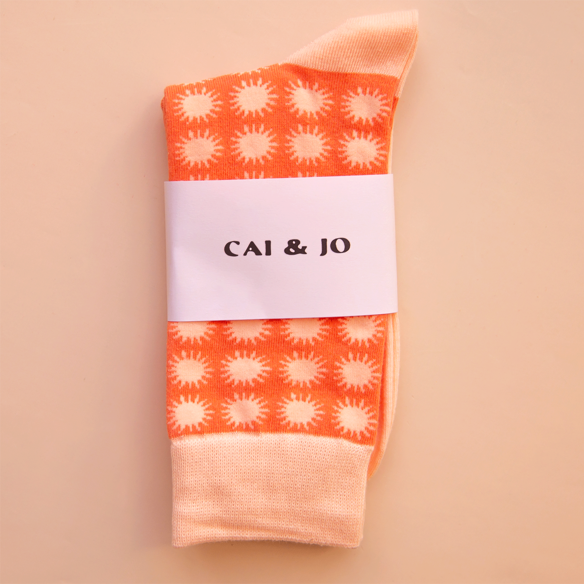 On a peach colored background is a pair of sunshine printed socks with an orange and light pink colorway.