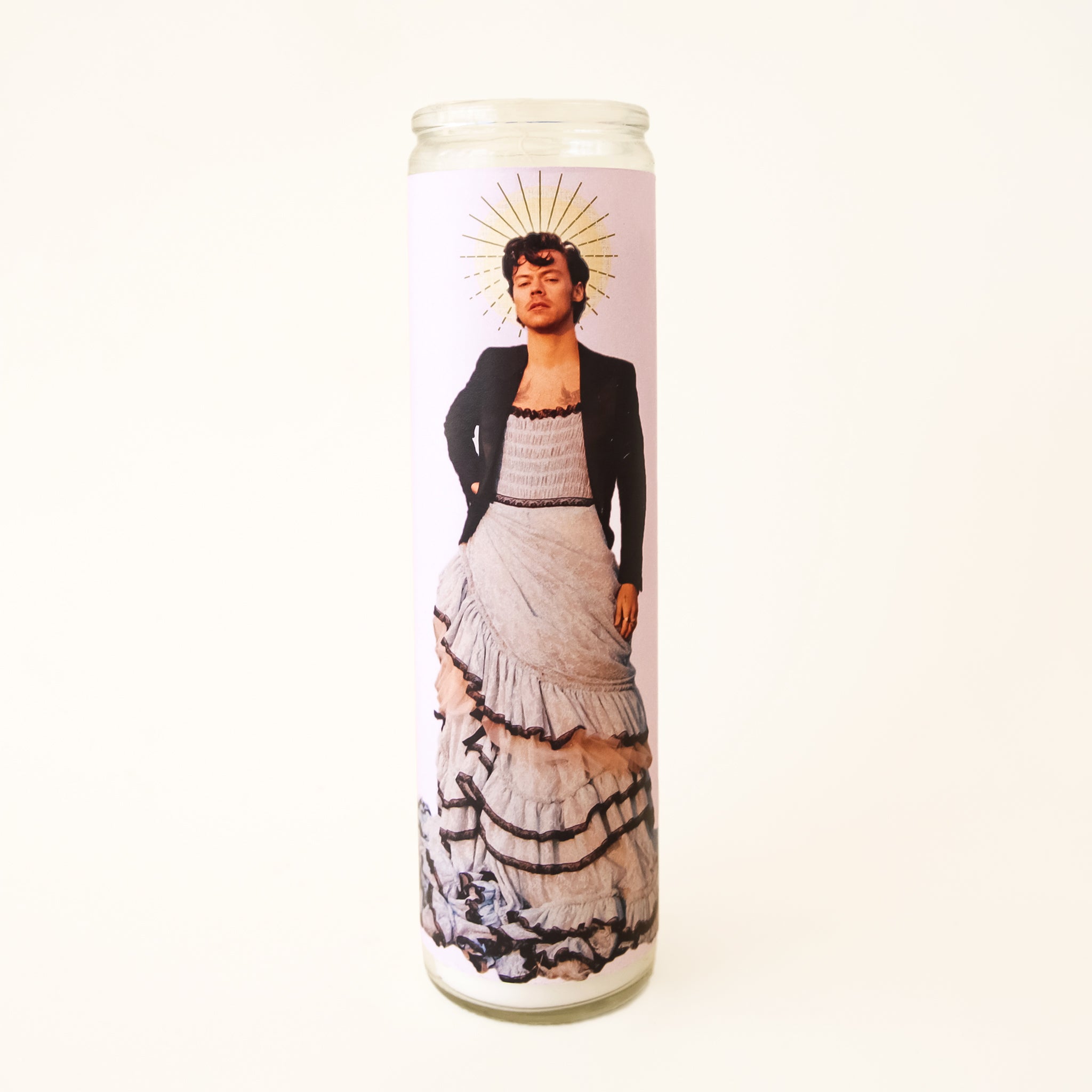 On a white background is a prayer candle with Harry Styles in a dress on the front. 