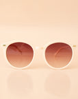 A white pair of rounded sunglasses with a brown lens. 