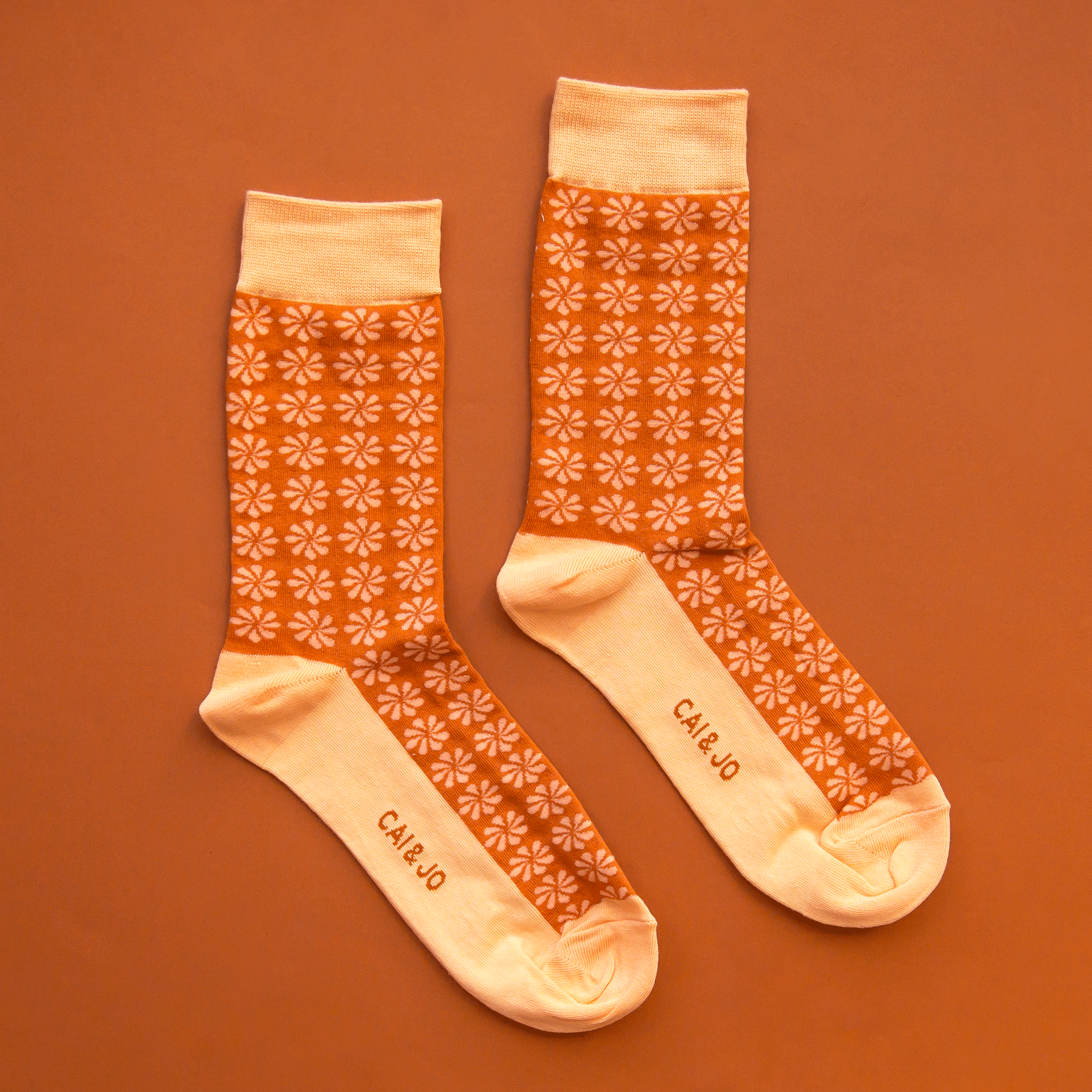 On an orange background is a pair of orange and light orange socks with a daisy print on them.