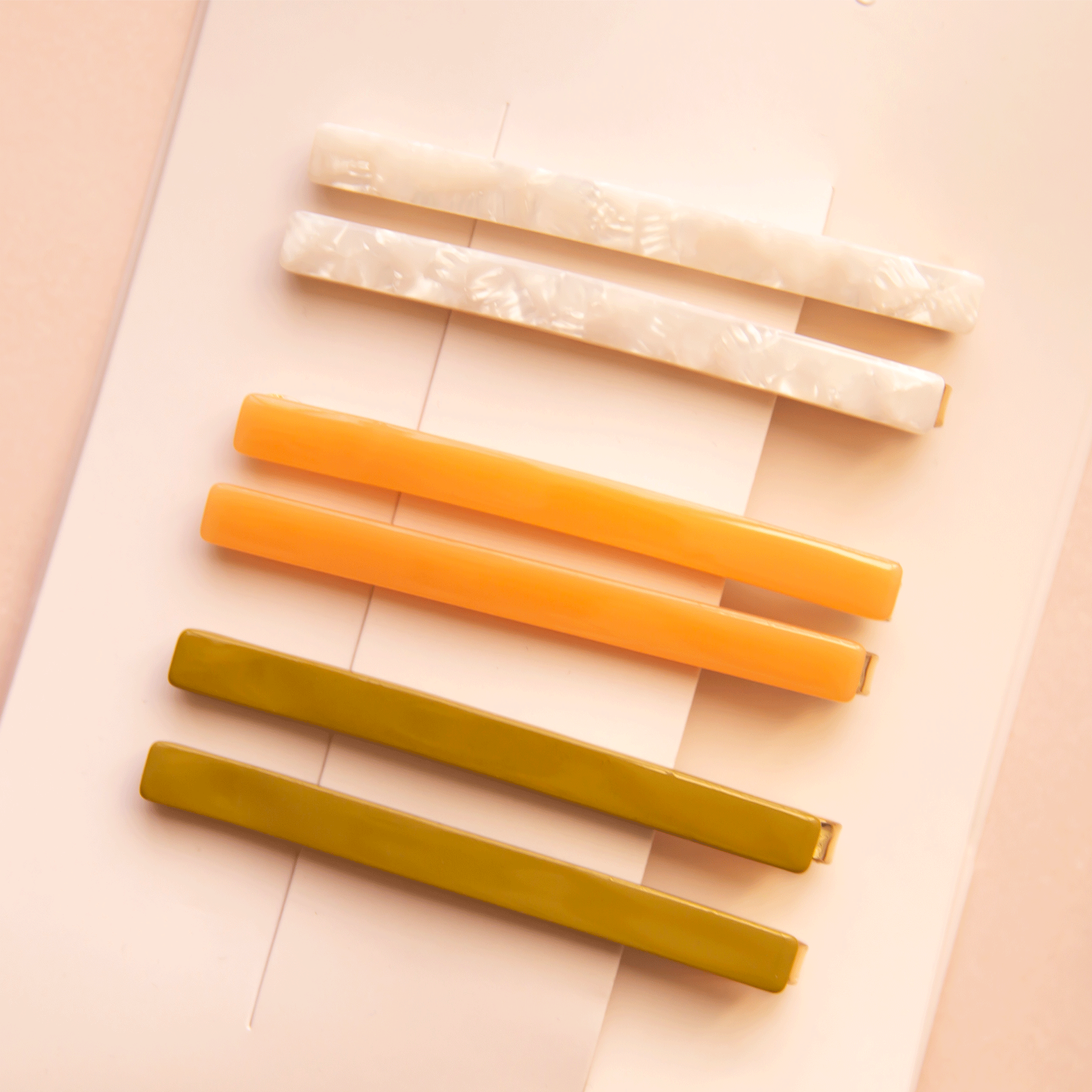 On a white packaging is six bobby pin clips in three different colors. From top to bottom is an ivory shell shade, mango orange, and olive green shade. 
