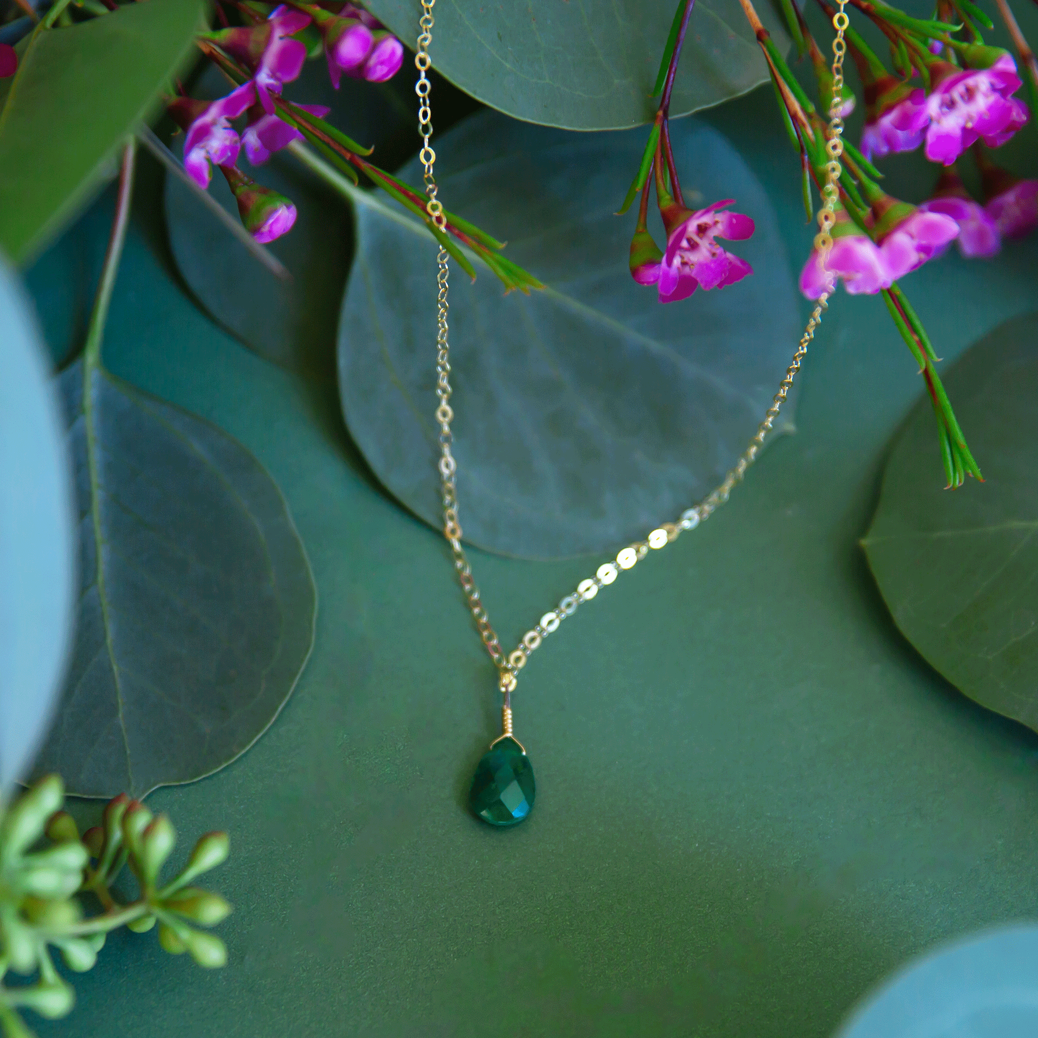 A gold chain necklace with a emerald stone charm in the center.