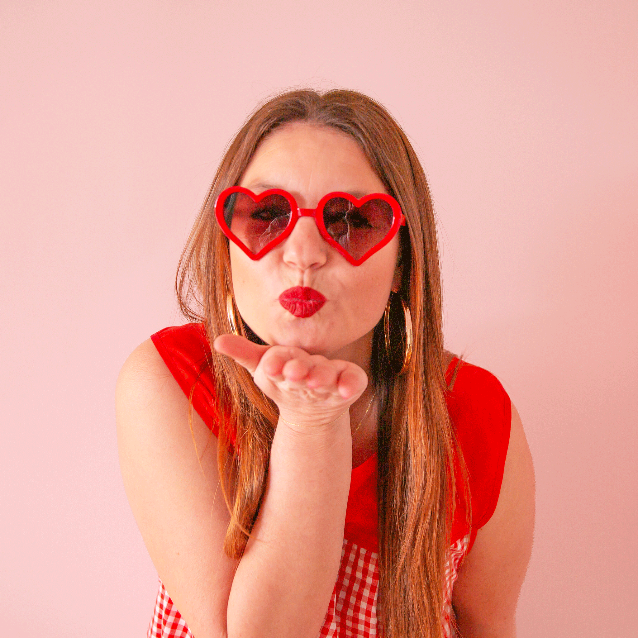 On a pink background is a model wearing the red heart shaped sunglasses. 