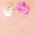 On a pink background is a pair of dainty gold hoop earrings. 