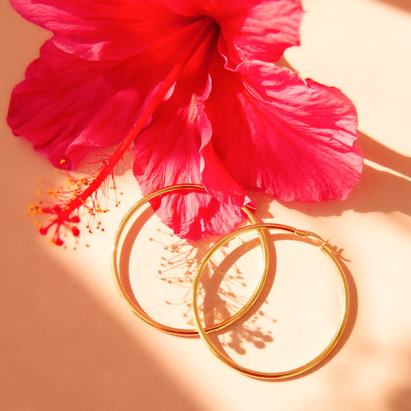 Gold hoops shown on a pink background with purple orchid flowers. 