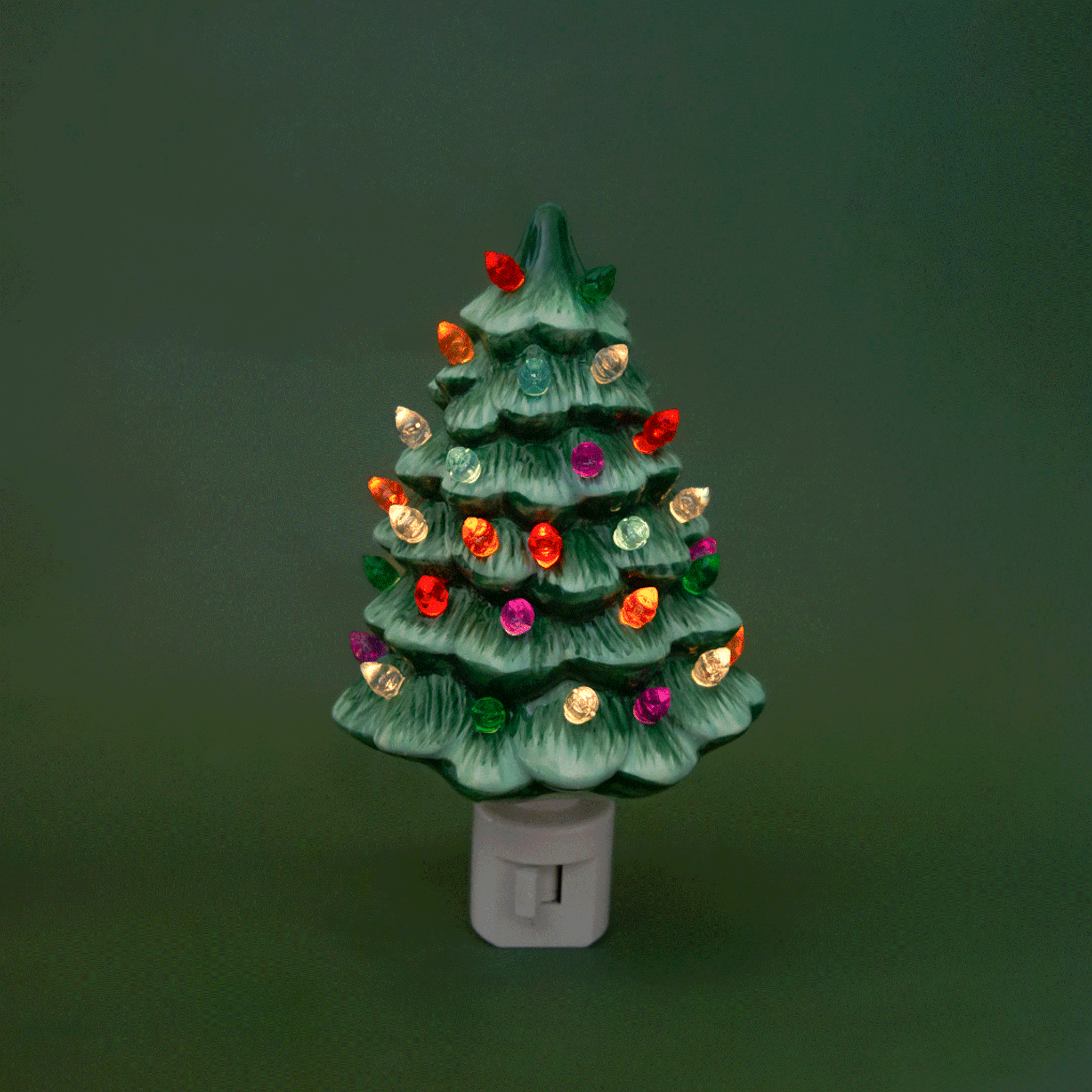 A ceramic Christmas Tree shaped night light sits in middle of the page with bright colorful lights.  It has a white plug at the bottom.  The tree is a green color.