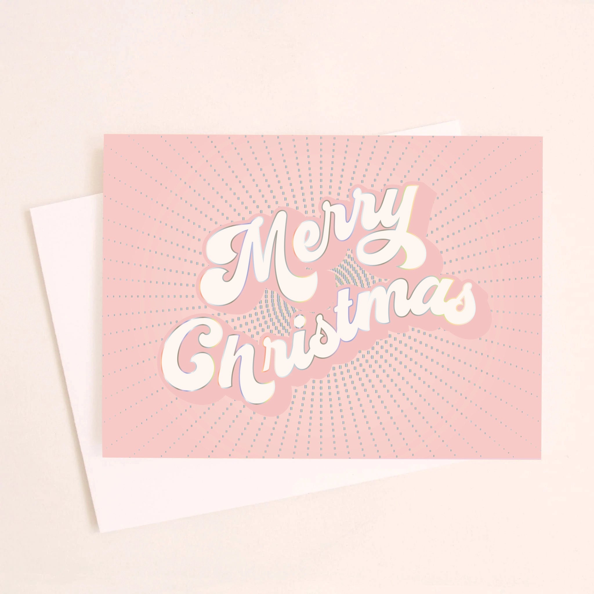 On a light pink background is a light pink greeting card with white text in the center that reads, "Merry Christmas" along with a white envelope.