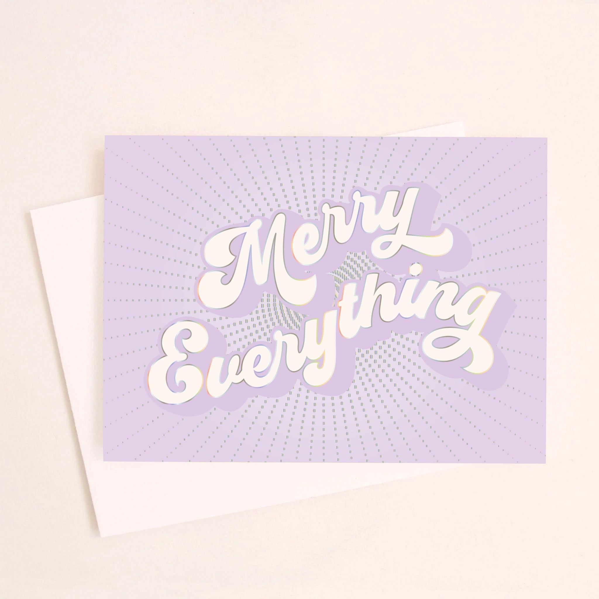 On a light pink background is a purple greeting card with white text that reads, "Merry Everything" along with a white envelope.