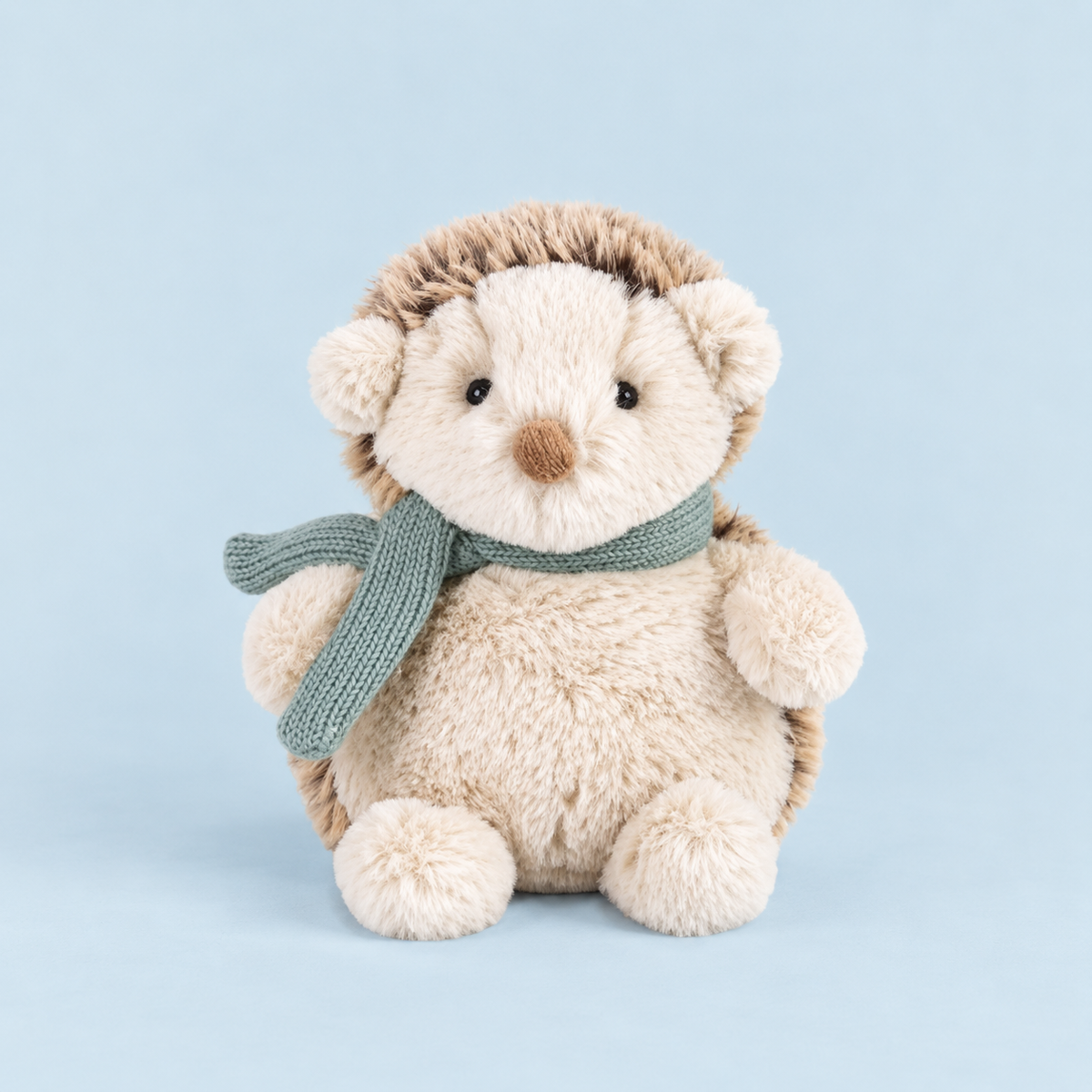 A neutral hedgehog shaped stuffed animal toy with a light teal colored scarf around its neck. 