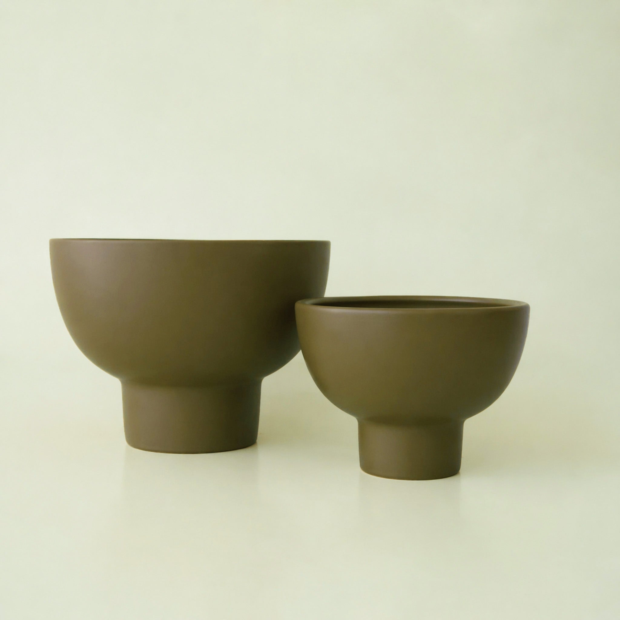 An olive green ceramic pedestal planter. 