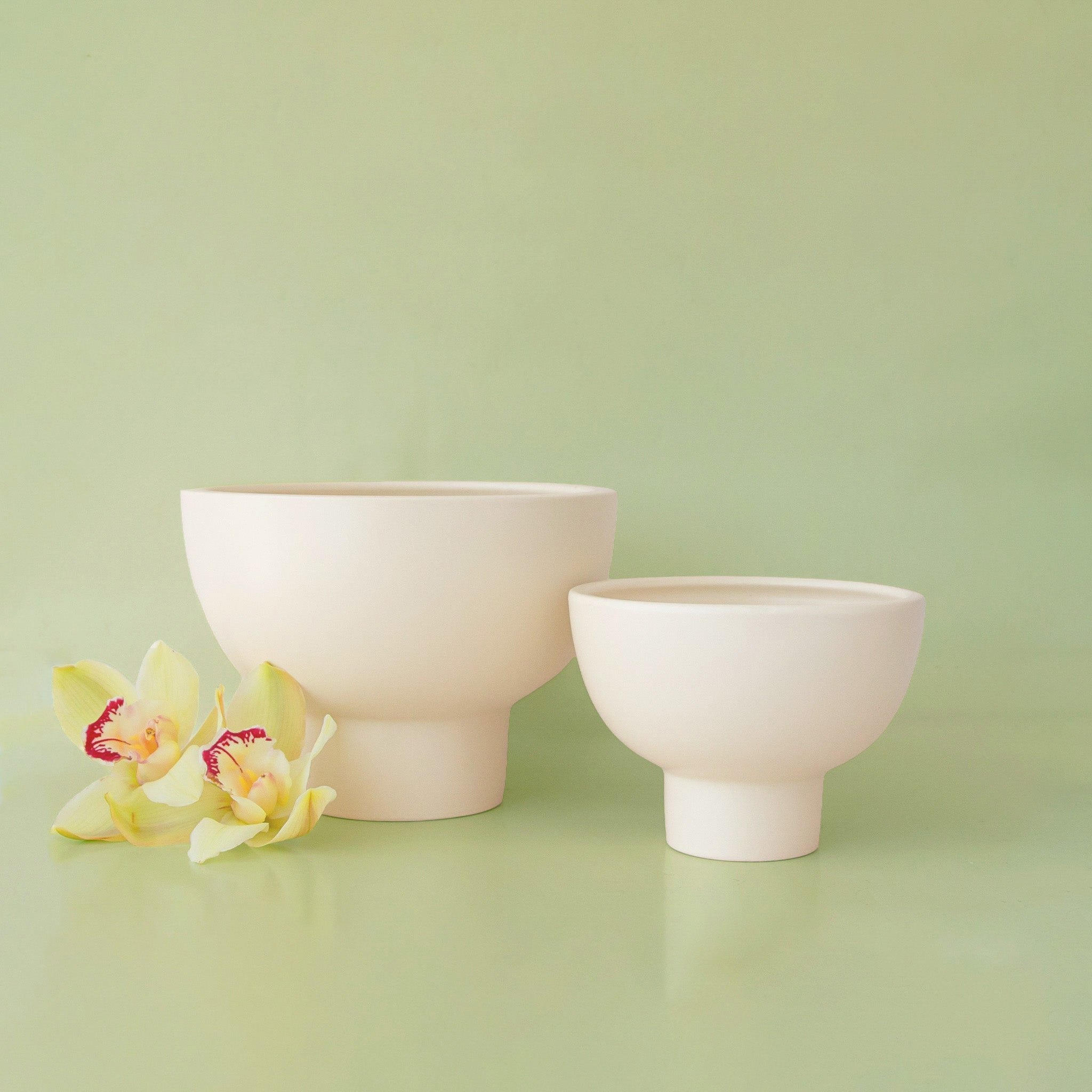 Two ceramic bowls on a light green background with a small orchid flower.