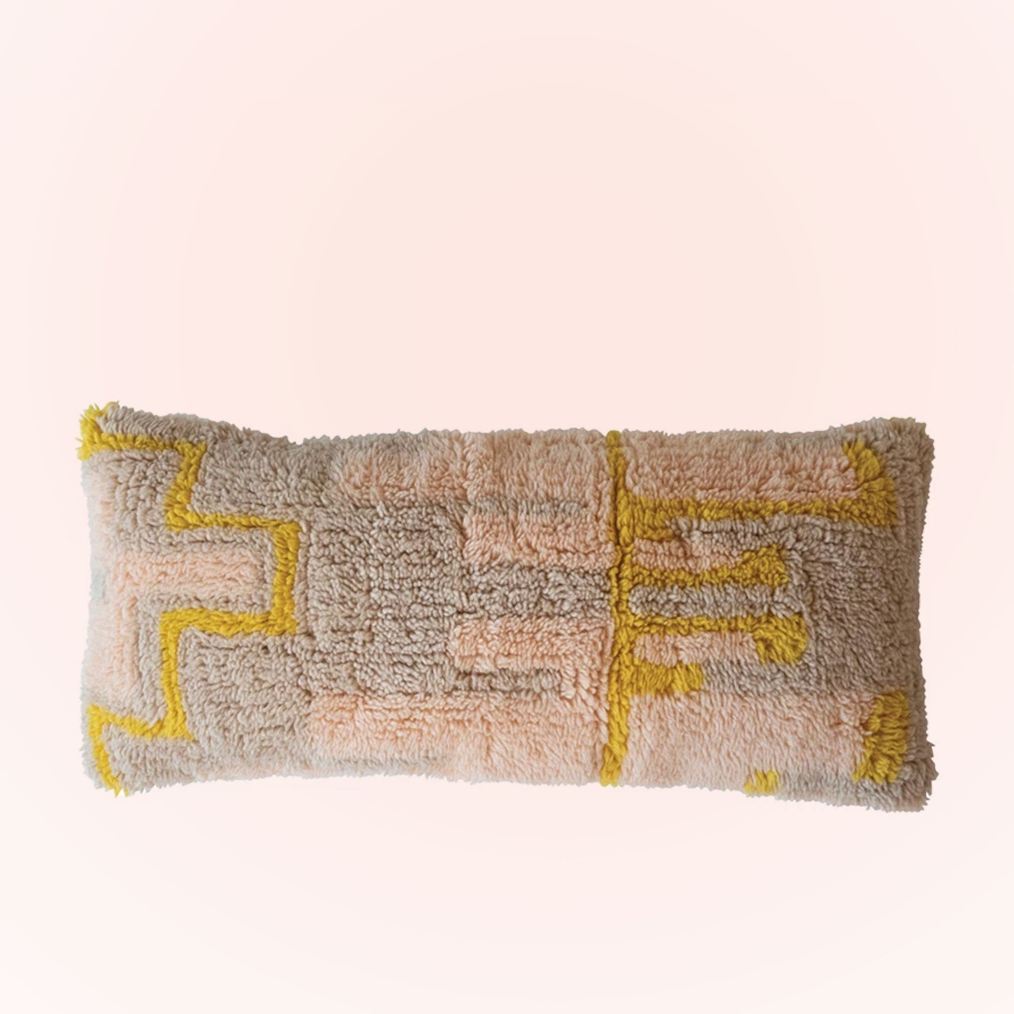 On a pink background is a tan, pink and yellow geometric printed lumbar pillow. 