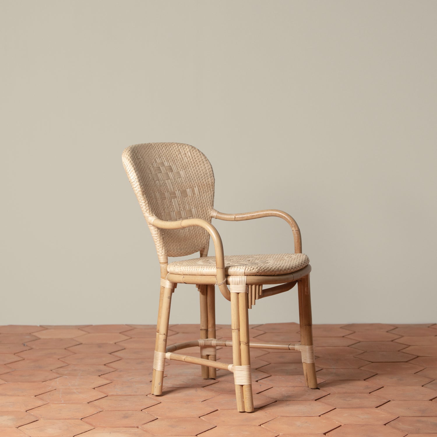 On an ivory background is a rattan chair with a woven rattan seat and backrest. 