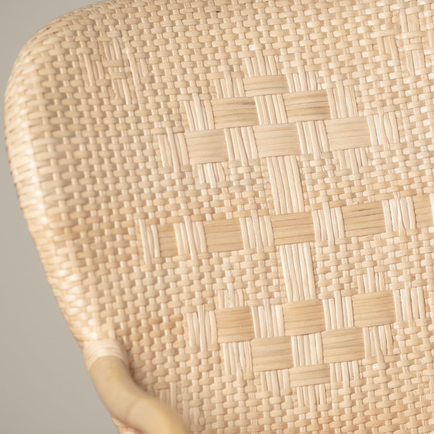 On an ivory background is a rattan chair with a woven rattan seat and backrest. This photo has a close up of the cane detailing. 