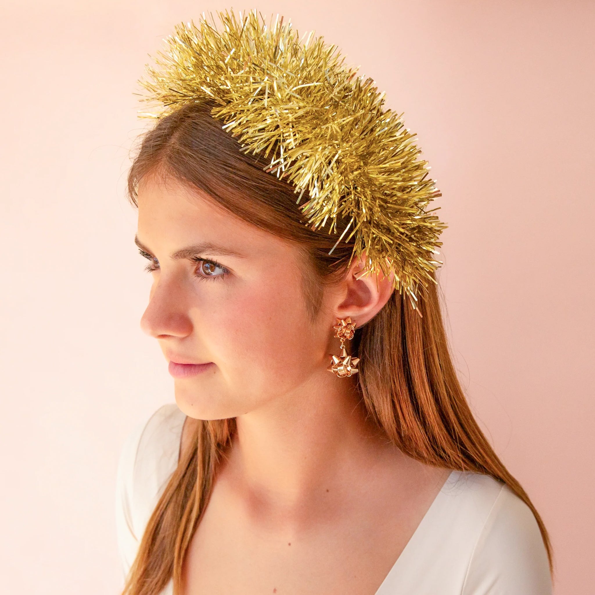 A gold tinsel headband worn by a model wearing gold bow shaped earrings.
