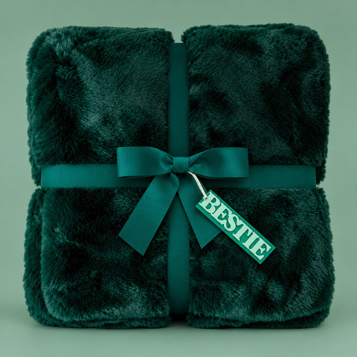An emerald fur blanket with a satin ribbon and a mint tag that reads "bestie" tied onto it.