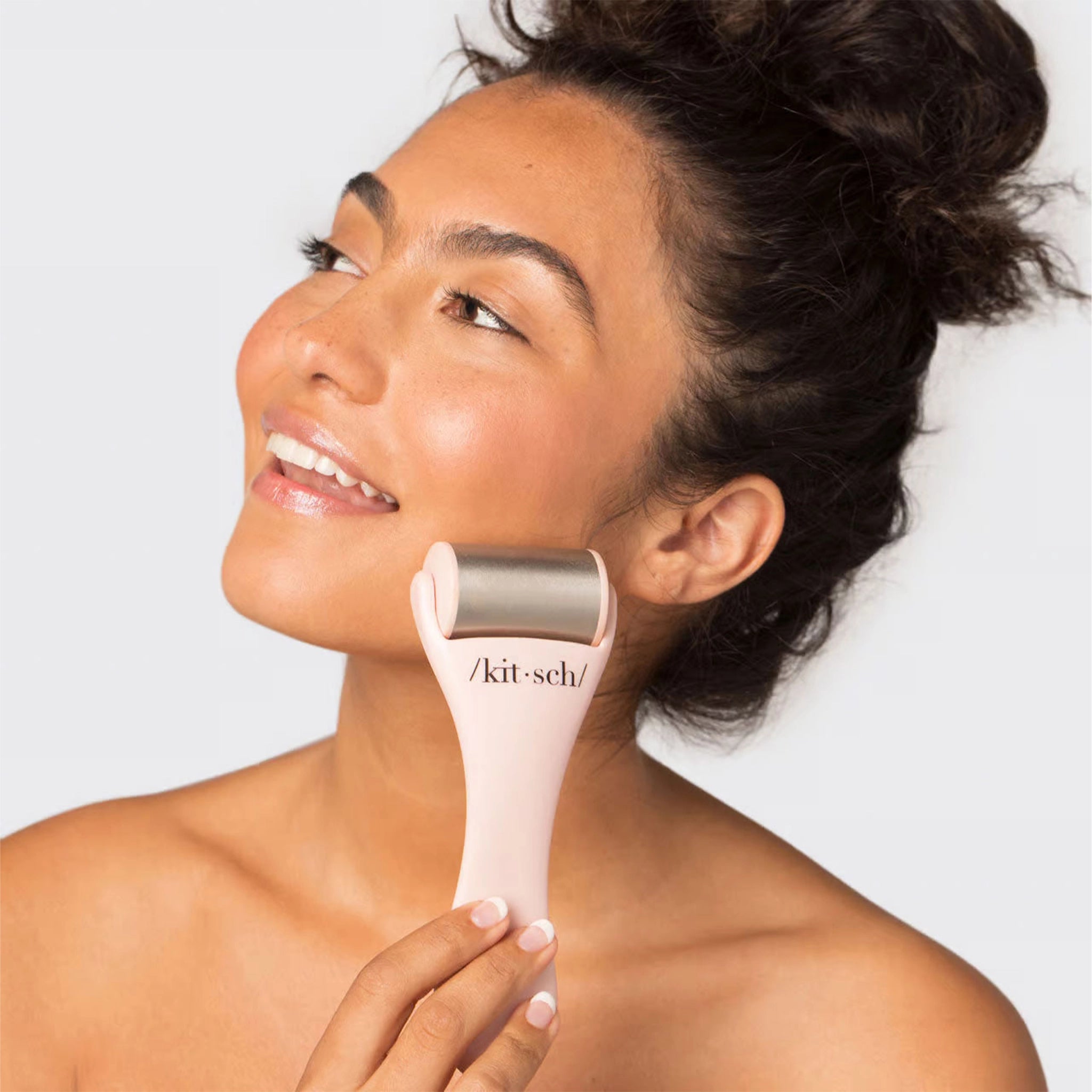 On a white background is a model holding a light pink and stainless steel facial ice roller.