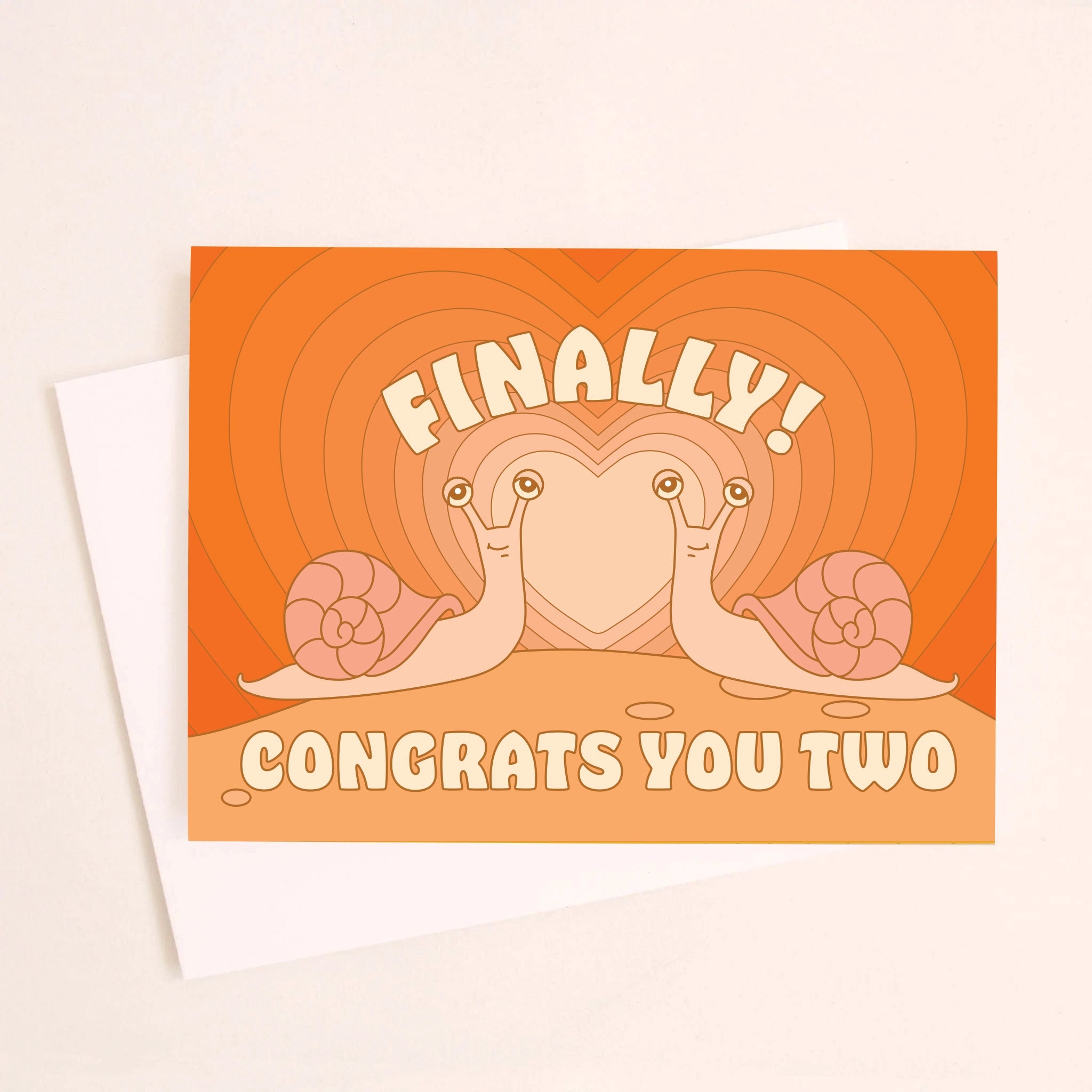 On an ivory background is a greeting card with an orange gradient heart card background with two snails coming towards one another and text above and below that reads, &quot;Finally Congrats You Two&quot;.