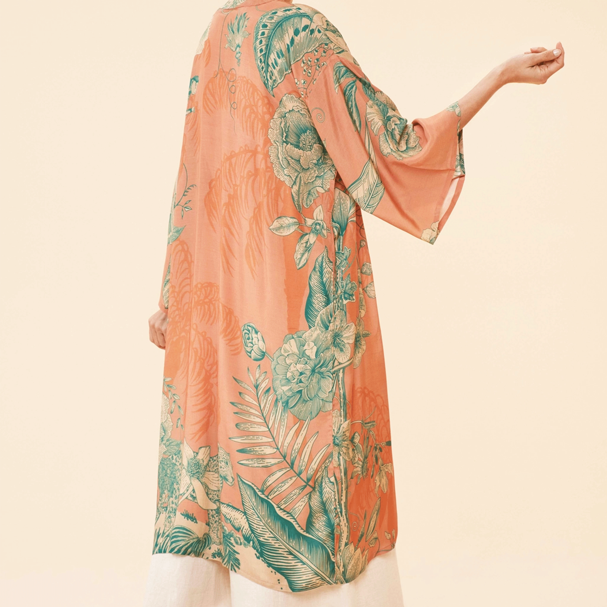 On a tan background is a model wearing an orange and teal kimono robe. 