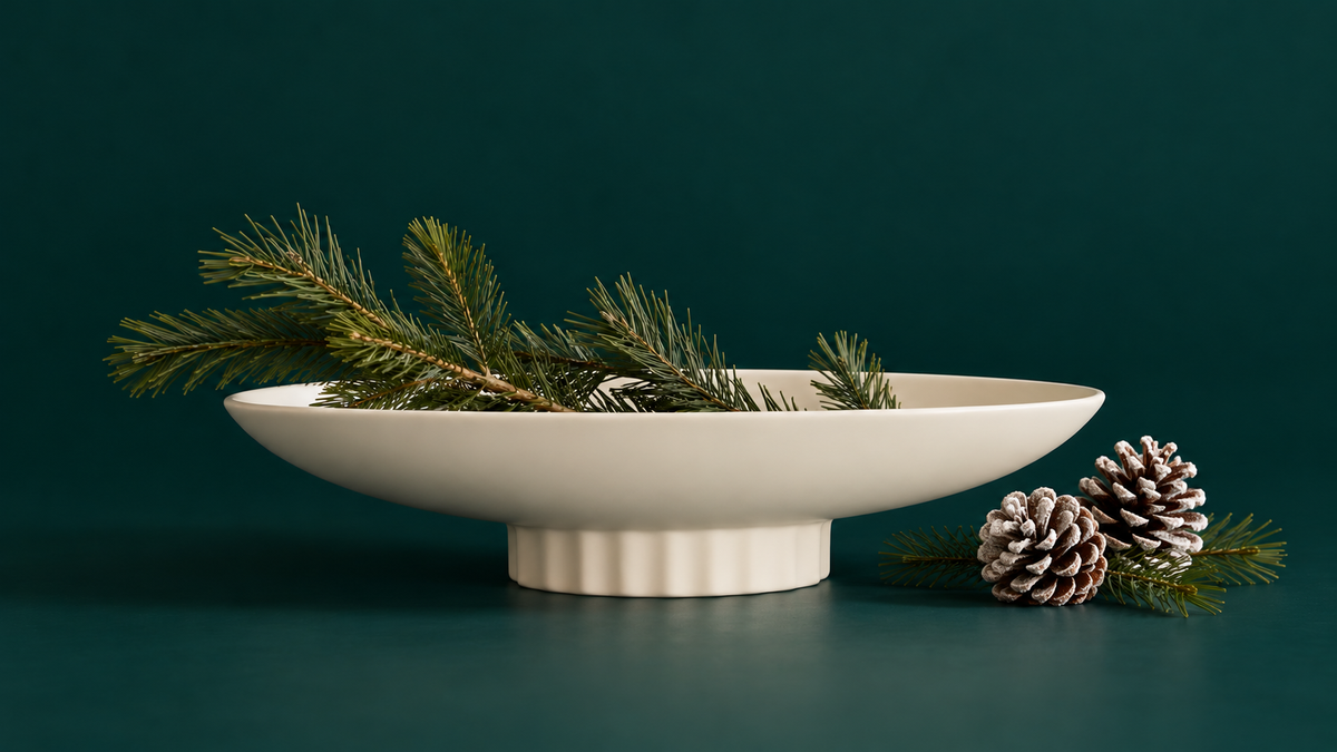 a white ceramic bowl holding a minimal pine branch arrangement. 